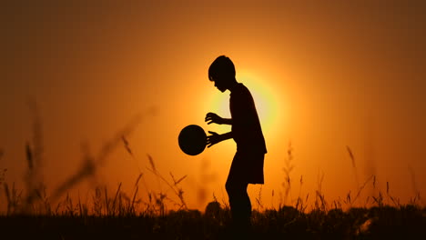 Silhouette-Eines-Jungen,-Der-Am-Strand-Football-Oder-Fußball-Spielt,-Mit-Wunderschönem-Sonnenuntergang-Im-Hintergrund,-Sportliches-Lifestyle-Konzept-Für-Die-Gelassenheit-Der-Kindheit.